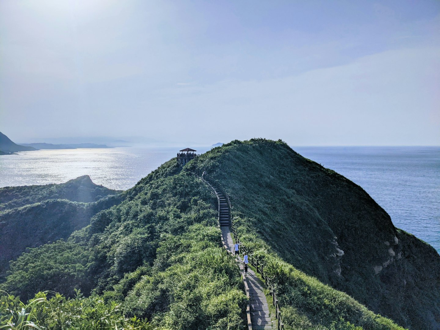 People walk up a stone path toward a coastal viewpoint.