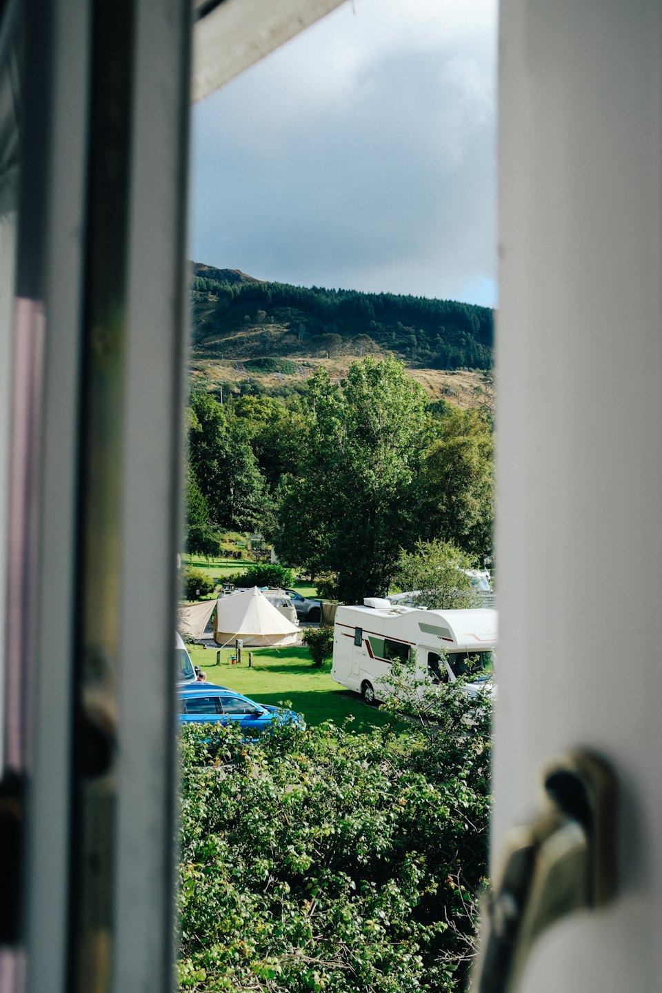 Motorhomes and tents parked on a grassy campground near hills.