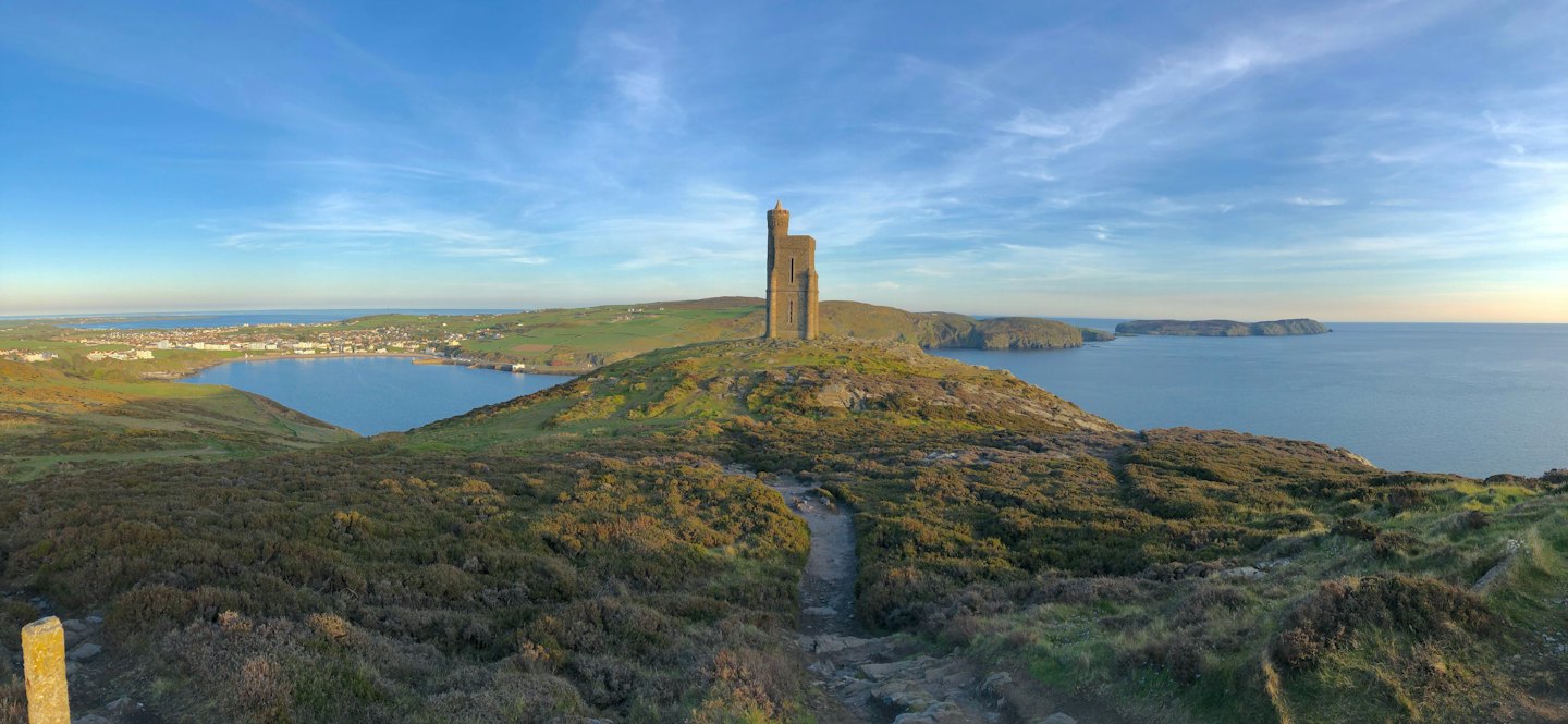 An old stone tower overlooks a coastal town by the sea.