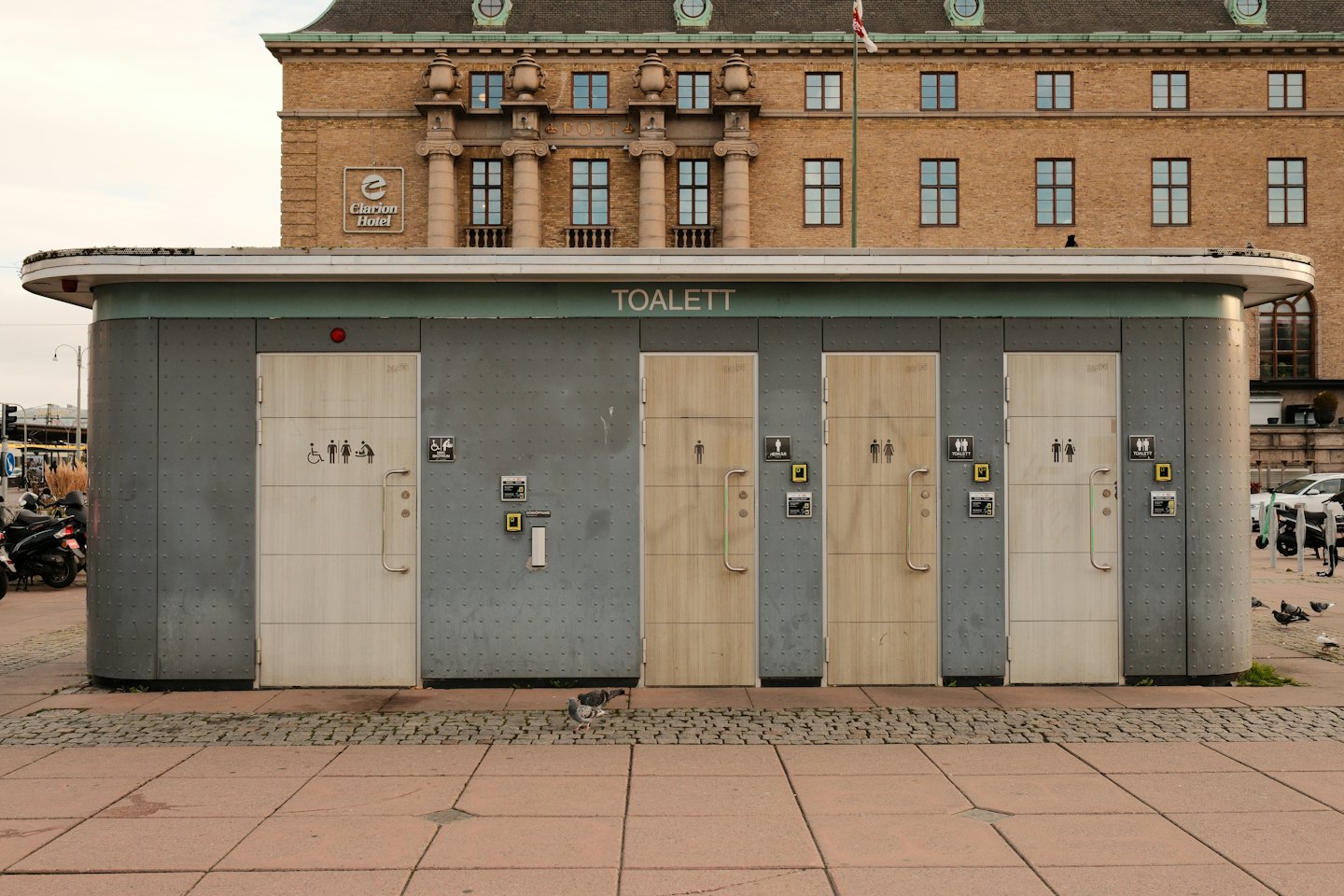 Modern grey public toilet block with beige doors and pictograms.