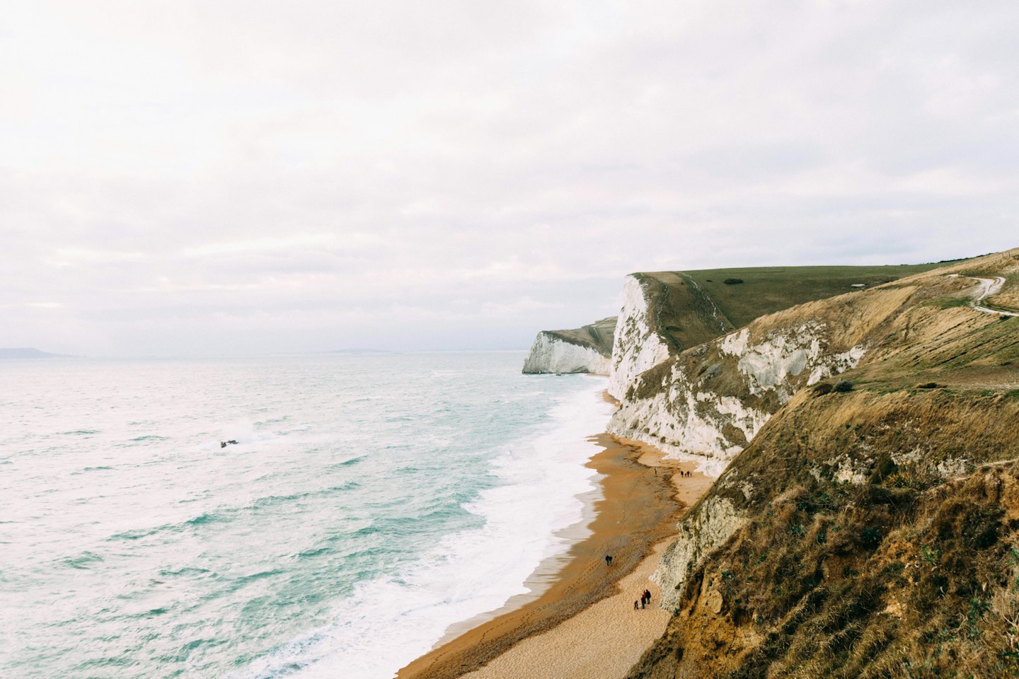 White chalk cliffs meet a foamy sea on a pebbled beach.