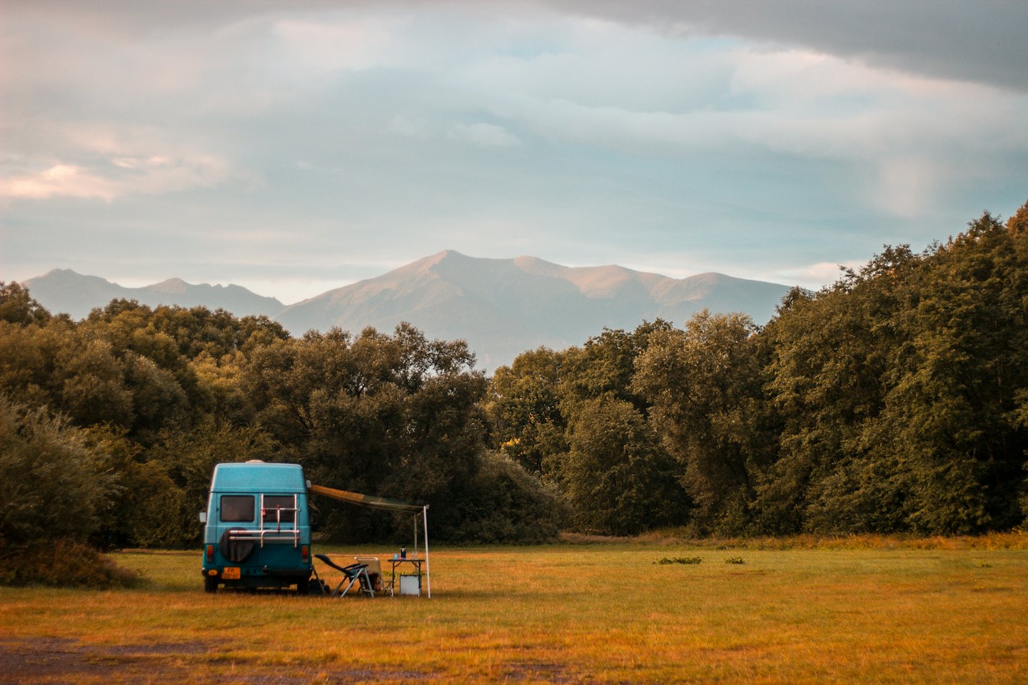 Light blue campervan with awning extended in grassy field.