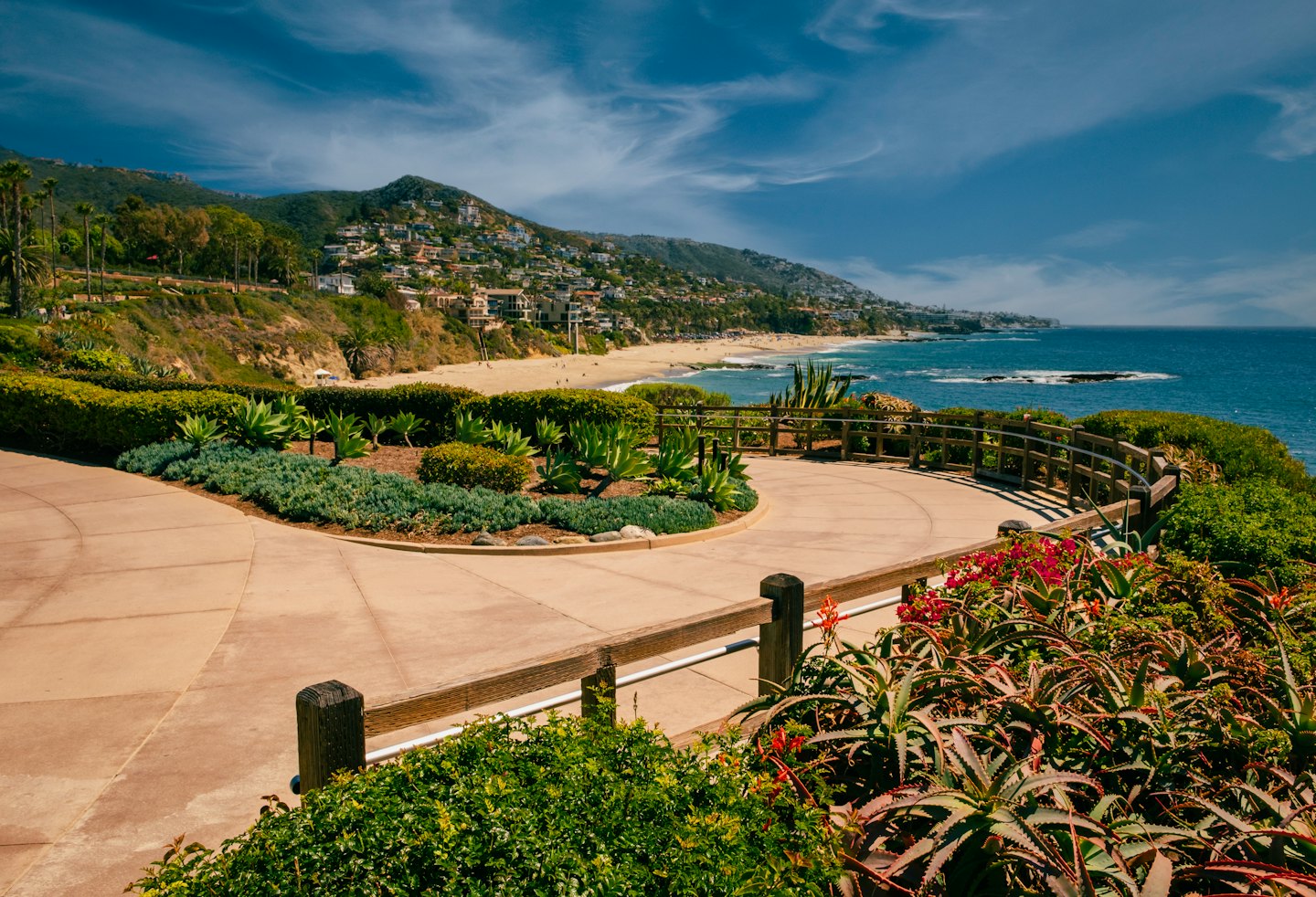 Sunny coastal walkway with railing overlooking a turquoise ocean.