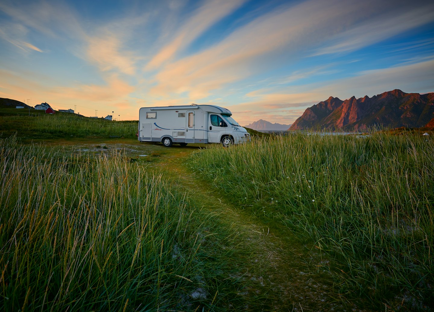 Campervan parked in grassy field with mountains at sunrise.